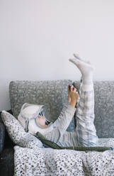Niedliches Kind im Schlafanzug auf der Couch liegend, während es zu Hause mit einer Videospielkonsole spielt - ADSF40325
