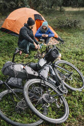 Radfahrer, die sich mit warmer Kleidung auf dem Lager ausruhen und nachts auf der grünen Wiese warme Getränke zu sich nehmen - ADSF40328
