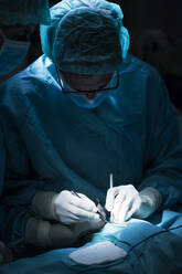 Man in surgeon uniform and his assistant performing surgery in dark operating theater - ADSF40351