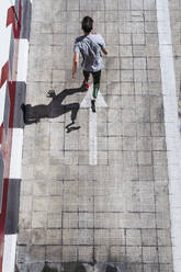 From above young guy with leg prosthesis running up paved slope against shabby building during workout on city street - ADSF40362