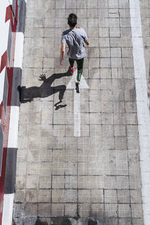 Von oben: Junger Mann mit Beinprothese, der während des Trainings auf einer städtischen Straße einen gepflasterten Abhang hinaufläuft und gegen ein schäbiges Gebäude prallt - ADSF40362