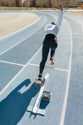 Rückenansicht einer nicht erkennbaren Sportlerin, die während eines Leichtathletik-Trainings im Stadion schnell aus den Startblöcken zu laufen beginnt - ADSF40367