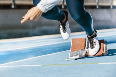 Abgeschnittene unerkennbare Sportlerin, die beginnt, schnell von den Startblöcken während des Leichtathletiktrainings im Stadion zu laufen - ADSF40369