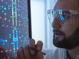 Scientist wearing protective eyeglasses analyzing DNA data on computer in laboratory - ABRF01019