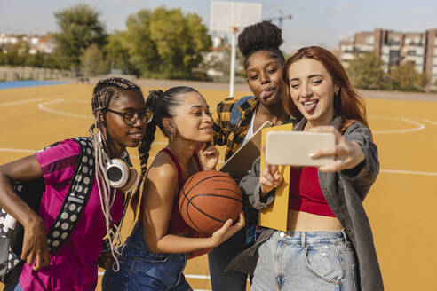 Glückliche junge Frau mit Freunden, die ein Selfie mit ihrem Smartphone auf dem Sportplatz machen - JCCMF07863