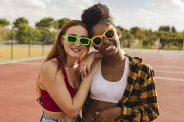 Junge Frauen mit Sonnenbrillen auf einem Sportplatz - JCCMF07903