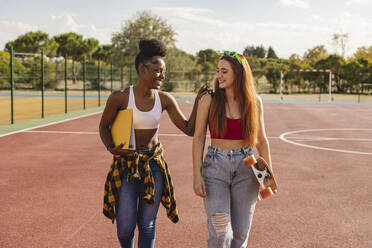 Glückliche Freunde gehen mit Skateboard und Feile in Sportplatz am sonnigen Tag - JCCMF07912