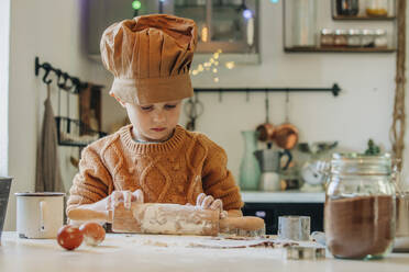 Boy preparing cookie dough with rolling pin at table - VSNF00119