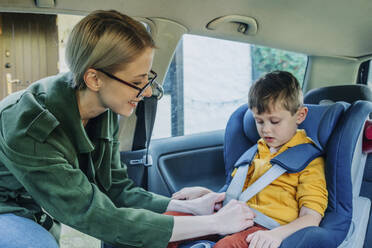 Happy mother fastening seat belt over son sitting in car - VSNF00121