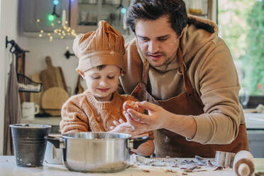 Lächelnder Sohn kocht mit Vater, der ein Ei am Küchentisch hält - VSNF00122
