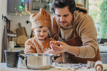 Smiling son cooking with father holding egg at table in kitchen - VSNF00122