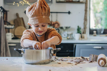 Smiling boy wearing chefs hat preparing food in utensil at home - VSNF00124