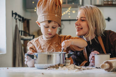 Happy blond woman with son preparing cookies on table at home - VSNF00126