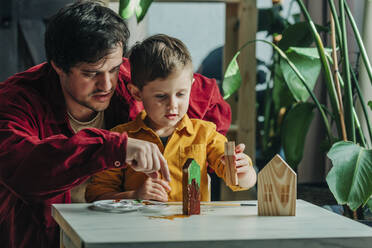 Father and son painting wooden houses together at home - VSNF00134