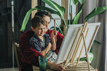 Glücklicher Vater und Sohn mit Pinsel und Blick auf die Leinwand - VSNF00139