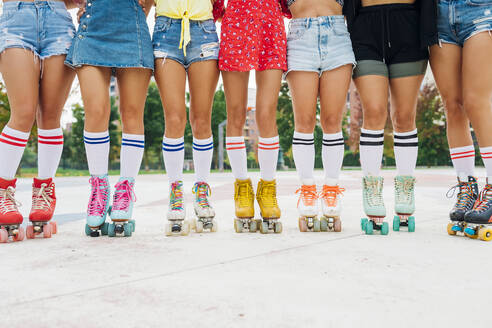 Legs of women wearing roller skates standing side by side at sports court - MEUF08435