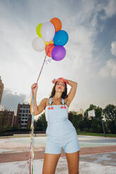 Junge Frau hält bunte Luftballons auf dem Sportplatz - MEUF08491