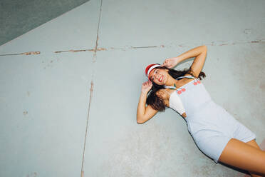 Glückliche Frau mit Sonnenblende auf dem Boden liegend auf einem Sportplatz - MEUF08496