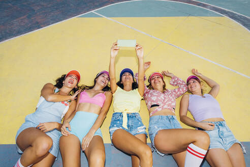 Happy woman with friends watching mobile phone lying on sports court - MEUF08512