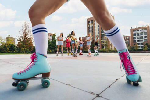 Friends wearing roller skates at sports court seen through woman's leg - MEUF08514