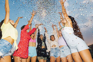 Happy friends throwing confetti under sky at dusk - MEUF08548