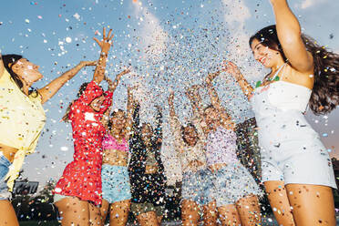 Happy female friends throwing confetti under sky at dusk - MEUF08549