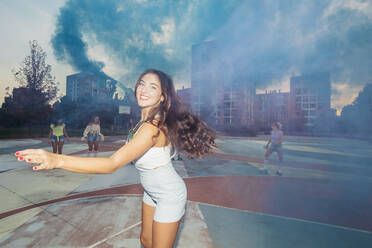 Happy woman with blue distress flare enjoying at sports court - MEUF08564