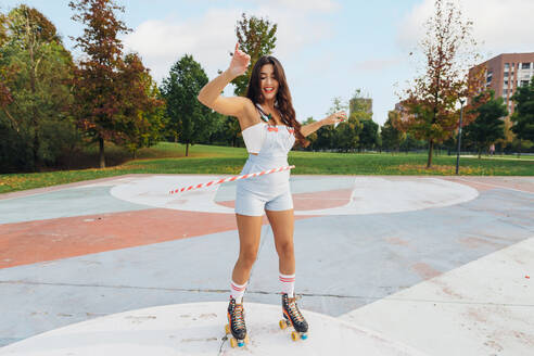 Happy woman wearing roller skate hula hooping at sports court - MEUF08573