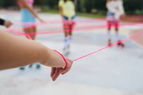 Hands of woman with friends holding pink string at sports court - MEUF08578