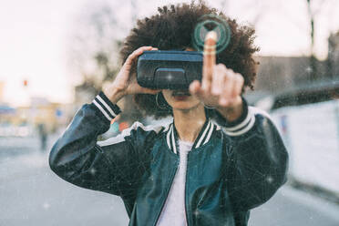 Junge Frau mit Afrofrisur trägt eine VR-Brille vor einem transparenten Bildschirm - MEUF08581