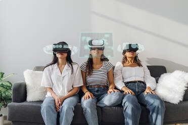 Friends wearing virtual reality glasses sitting on sofa at home - MEUF08595