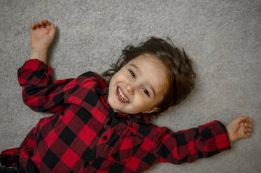 Niedlicher glücklicher Junge im karierten Hemd auf dem Teppich liegend - ANAF00509