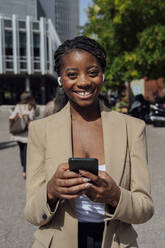 Glückliche Geschäftsfrau mit Smartphone auf dem Fußweg stehend - PGF01326
