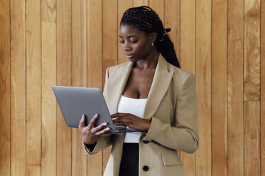Geschäftsfrau mit Laptop vor einer Holzwand - PGF01343