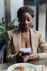 Lächelnde Geschäftsfrau, die in der Cafeteria eine Textnachricht auf ihrem Smartphone schreibt - PGF01357
