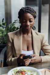 Smiling businesswoman text messaging on smart phone at cafeteria - PGF01357