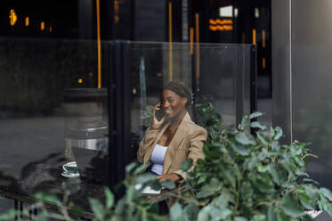 Lächelnde Geschäftsfrau, die mit ihrem Handy telefoniert, gesehen durch das Glas einer Cafeteria - PGF01362