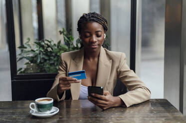 Businesswoman with credit card and smart phone sitting at cafe - PGF01369