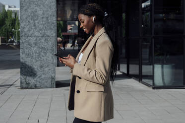 Geschäftsfrau benutzt Smartphone beim Gehen auf dem Fußweg - PGF01376