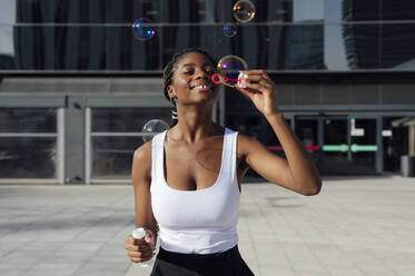 Young woman blowing bubbles outside building - PGF01380