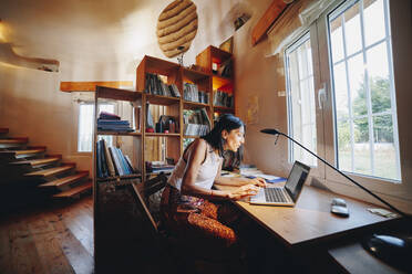 Reife Frau mit Laptop am Tisch sitzend im Haus - MRRF02520