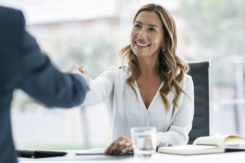 Happy businesswoman shaking hand with colleague in office - JSRF02267