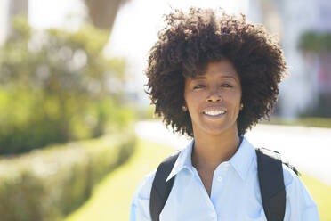Glückliche Studentin mit Afrofrisur an einem sonnigen Tag - JSMF02475