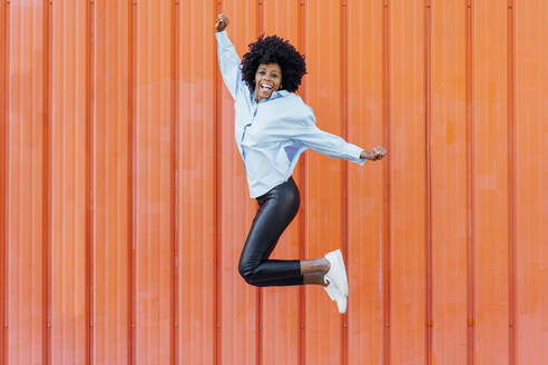 Unbekümmerte junge Frau, die vor einer orangefarbenen Wand springt - JSMF02479