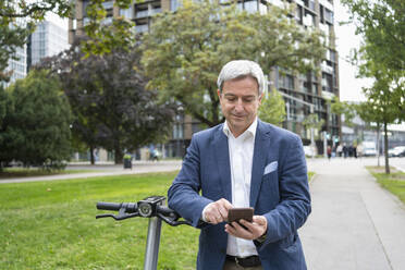 Lächelnder reifer Geschäftsmann, der sein Smartphone benutzt, um den Elektroroller zu entsperren - SVKF00724