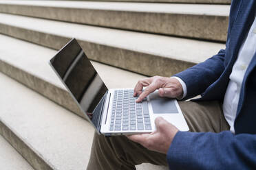 Hände eines Geschäftsmannes, der an einem Laptop arbeitet und auf einer Treppe sitzt - SVKF00739