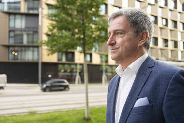 Thoughtful mature businessman in front of buildings - SVKF00755