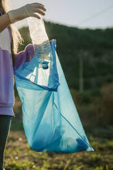 Woman putting plastic bottle in blue garbage bag - ACPF01531
