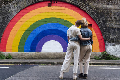 Ein schwules Paar steht zusammen vor einer regenbogenfarbenen Wand - ASGF03091