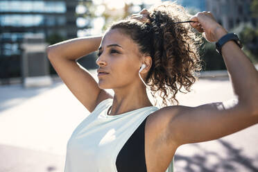 Young woman tying hair on sunny day - JSRF02281